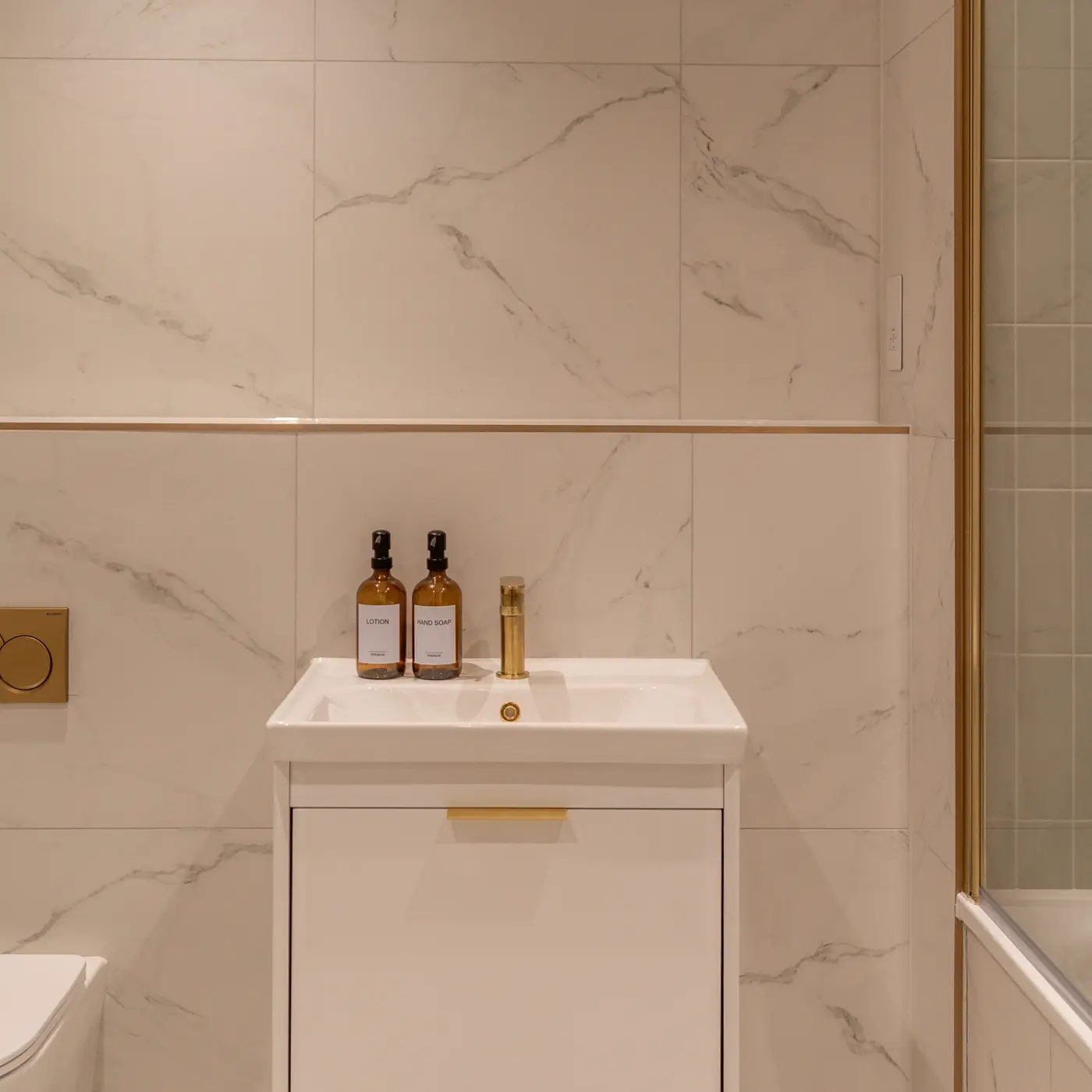 Shot of the main bathroom with the floating white sink basin with gold features. White marble tiling and gold features.